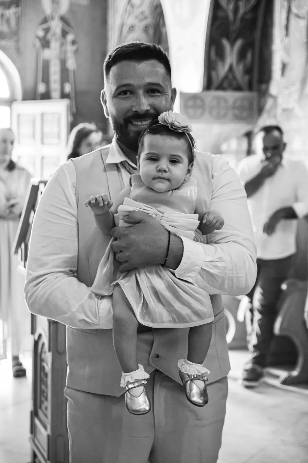Nasmejani tata sa bebom u naručju na krštenju, crno-bela fotografija